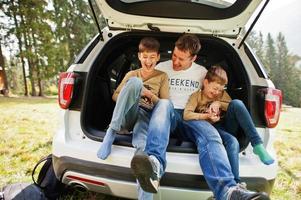 familie bij voertuiginterieur. vader met zijn zonen. kinderen in de kofferbak. reizen met de auto in de bergen, sfeerconcept. foto