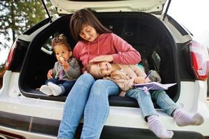 familie bij voertuiginterieur. moeder met haar dochters. kinderen in de kofferbak. reizen met de auto in de bergen, sfeerconcept. foto