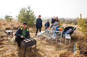 groot gezin met vier kinderen barbecueën op een terras in het dennenbos. bbq-dag met grill. foto