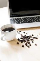 een kopje koffie, laptop en verspreid koffiebonen foto