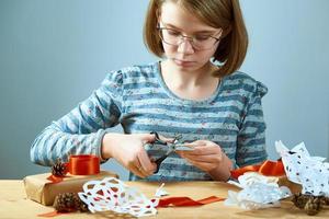 meisje tiener met bril sneeuwvlokken uit papier snijden. conceptvoorbereiding voor het nieuwe jaar. foto