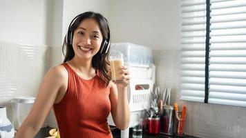mooie jonge vrouw die smoothies maakt en drinkt van fruit in de keuken thuis terwijl ze naar muziek luistert via een koptelefoon - lifestyle concepten foto