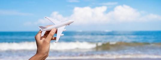 hand met een miniatuurvliegtuig op het tropische strand op een zonnige dag, zomervakantie en reisconcept foto