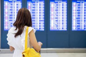 jonge vrouwelijke reiziger op de luchthaven die naar het vluchtinformatiebord kijkt foto