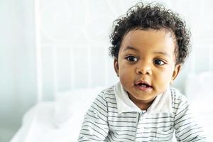 schattige Afrikaanse baby met pluizig haar op het bed, mooie jongen foto