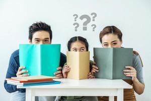 portret van schattige aantrekkelijke mooie Aziatische familie, Aziatische jonge moeder en vader met dochtertje en vraagteken boven het hoofd zitten aan het bureau en houden boek met grappige gezichtsuitdrukking foto