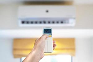 airconditioner in de kamer, man's hand met behulp van afstandsbediening opent de airconditioner in zijn slaapkamer. gezondheidsconcepten en energiebesparing foto