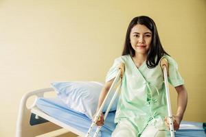 portret van gelukkige jonge vrouwelijke patiënt zittend in bed met krukken in een ziekenhuiskamer. gezondheidszorg en medische verzekering concept. foto