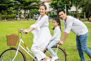 gelukkige familie met fiets buiten op zomerdag, Aziatische vader en moeder met dochter genieten van fietsen buiten in een park. foto