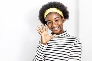 schattig afro-amerikaans meisje dat vrijetijdskleding draagt en zwaait en zegt hallo blij en glimlachend, vriendelijk welkom gebaar foto