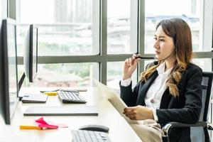 doordachte jonge aziatische vrouw die denkt met behulp van zakelijke visie in de buurt van laptop voor het berekenen van financiële tarieven die naar de toekomst op kantoor kijken. meisjesboekhouding met cheque kredietanalyse voor hypotheekbetaling foto