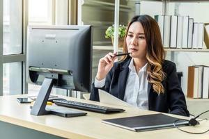 doordachte jonge aziatische vrouw die denkt met behulp van zakelijke visie in de buurt van laptop voor het berekenen van financiële tarieven die naar de toekomst op kantoor kijken. meisjesboekhouding met cheque kredietanalyse voor hypotheekbetaling foto