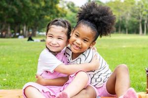 twee Afro-Amerikaanse vrolijke kleine meisjes zitten op de mat en knuffelen elkaar met liefde in de tuin foto