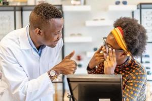 man professionele opticien helpt en verkoopt jonge vrouw Afro-Amerikaanse brillenglazen in opticienwinkel. juiste hulp of gebrekkig gezichtsvermogen gebruikt. foto