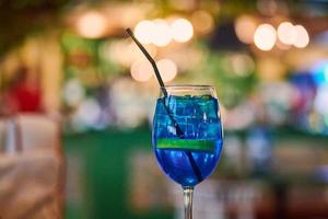 blauwe lagune cocktaildrank in glas met stro, nacht café licht bokeh achtergrond kopie ruimte foto