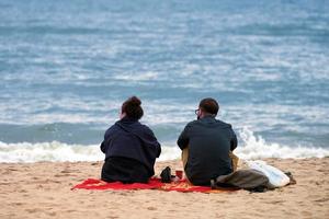 romantisch picknick liefdespaar zittend op zee strand, openhartig paar pratend over romantische relatie foto