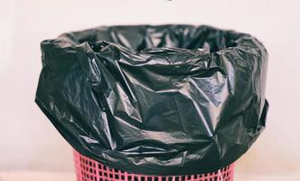 afvalbak, afvalafval en zak plastic zwart - prullenbak op muurachtergrond foto