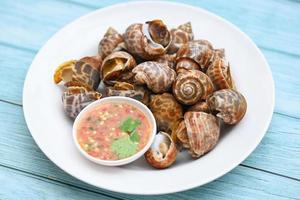 vers gevlekte babylon zeeschelp limpet oceaan gastronomische zeevruchten in het restaurant, babylonia areolata schelpdieren zeevruchten op witte plaat met zeevruchten saus op tafel achtergrond foto