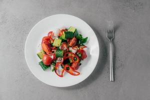 bovenaanzicht van verse groentesalade bereid van rode peper, radijs, tomaten, komkommers en peterselie in witte kom, vork in de buurt. vegetarisch gerecht concept. gezonde voedzame lentesalade foto