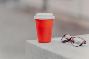 horizontale opname van rode koffie om te gaan en optische glazen. aromatische koffie om te drinken. drinkconcept. papieren kopje warme drank foto