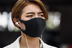 jonge aziatische vrouw die buiten gezichtsmasker draagt terwijl ze naar muziek luistert in de stad tijdens de covid-19 pandemie foto