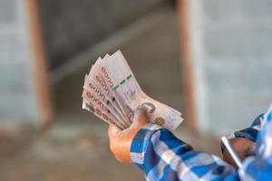 de handen van een bouwvakker die een bankbiljet vasthoudt ter waarde van 5.000 baht foto