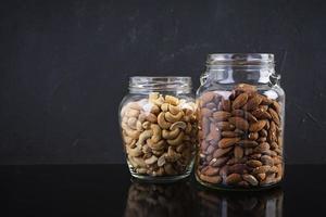 cashewnoten en amandelen noten in een pot. set van noten geïsoleerd op donkere achtergrond foto