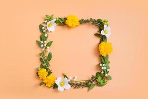 zomer of lente compositie op een oranje achtergrond. gele en witte bloemen en groene bladeren met een kopie ruimte krans bovenaanzicht. zomer, lente bloemen concept foto