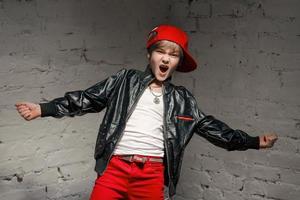 portret van een coole jonge hiphopjongen in een rode hoed en een rode broek en een wit overhemd en een zwart leren jack in de loft foto