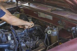 de hand van een man die de motor van een kapotte auto repareert foto