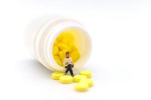 gezondheidszorg, medisch en informatieconcept. close-up van zakenvrouw miniatuur figuur zitten en lezen boek op fles gele pillen op witte achtergrond. foto