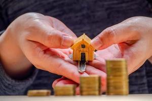 huis- of huismodel en munten bij de hand met huissleutel. concept voor lening, vastgoedladder, financieel, hypotheek, vastgoedinvestering, belastingen en bonus. foto