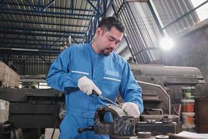 een professionele Aziatische mannelijke industrie-ingenieur werkt in een veiligheidsuniform met precisiegereedschappen voor metaalbewerking, mechanische draaimachines en een werkplaats voor reserveonderdelen in de staalfabriek. foto