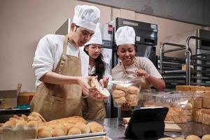 jonge start-uppartners van drie chef-koks, blogger voor kleine bedrijven livestreaming via mobiele applicatietechnologie, online promotie van bakkerijverkopen, vers brood, banketbakkerswaren en koken in commerciële keukens. foto