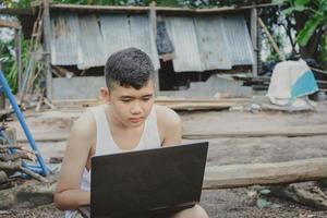 Aziatische jongen studeert online met laptop op zijn bureau thuis platteland, leren met leraar thuis, thuisonderwijs afstand leren online internet landelijk, slecht gebrek aan educatieve apparatuur foto