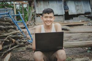 arme mannelijke student die online studeert met een gelukkige laptop glimlacht naar de camera. Aziatische jongens van basisschoolleeftijd die op het platteland wonen en scholen op het platteland van Thailand. foto
