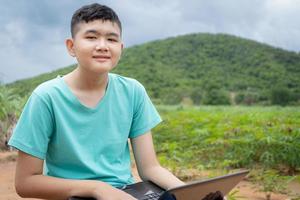 jongen die online studeert in de landelijke natuur en naar de camera kijkt foto