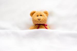 teddybeerpop liggend in het witte bed foto