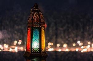 selectieve focus op blauwe spiegel van lantaarn met lichten die versieren voor islamitisch nieuwjaar bij raam met regendruppel op de achtergrond. foto