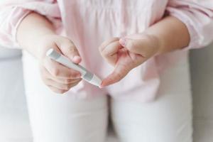 Aziatische vrouw die lancet op vinger gebruikt voor het controleren van de bloedsuikerspiegel door glucosemeter, gezondheidszorg en medisch, diabetes, glycemieconcept foto