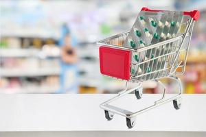 geneeskunde pillen capsule in winkelwagen op apotheek winkel teller met onscherpte drogisterij planken intreepupil achtergrond foto