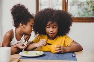 kleine schattige jongere zus ziet er interessant uit, haar oudere zus probeert groente te leren eten. foto