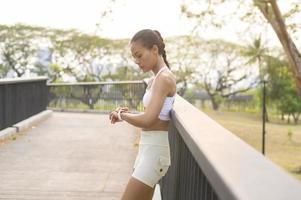 een jonge fitnessvrouw in sportkleding die een slim horloge gebruikt tijdens het sporten in het stadspark, gezond en levensstijl. foto