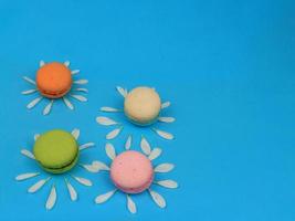 schattige madeliefje bitterkoekjes, kleurrijke franse macarons met chrysant bloemblaadje bloem, heerlijk zoet dessert op blauwe achtergrond met copyspace, voedsel achtergrond concept. foto