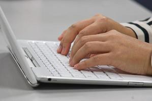 vrouw die aan het bureau zit te typen op het toetsenbord van een witte laptop foto