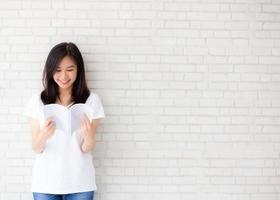 mooi van portret jonge aziatische vrouw geluk ontspannen staand leesboek op betonnen cement witte achtergrond thuis, meisje gelukkig studie inhoud literatuur, onderwijs en lifestyle concept. foto