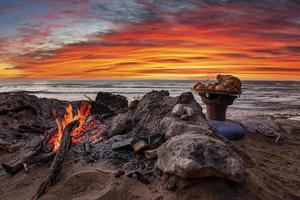 vers fruit in bord naast vreugdevuur met brandend brandhout op het strand bij zonsondergang foto