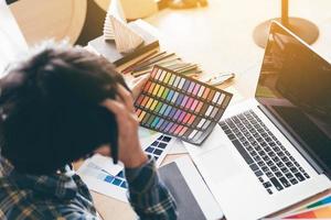 achteraanzicht van ontwerper die aan zijn bureau werkt met hoofdpijn over het kiezen van kleuren. foto