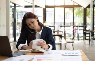 Aziatische vrouw die aan de telefoon werkt. een zakenvrouw is druk bezig met haar laptopcomputer en het berekenen van de informatie die je haar op kantoor noemt. foto