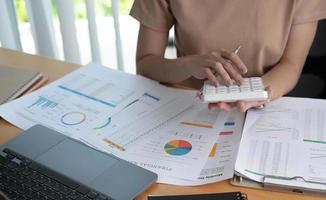 close-up van zakenvrouw of accountant die rekenmachine gebruikt om bedrijfsgegevens te berekenen, werken op kantoor met papieren document en laptopcomputer op kantoortafel, bedrijfs- en financieel concept foto